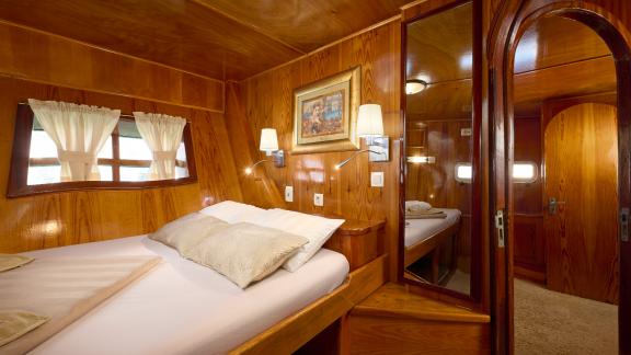 An elegant cabin on the Gulet Linda with a single bed, wooden panelling and a mirror.